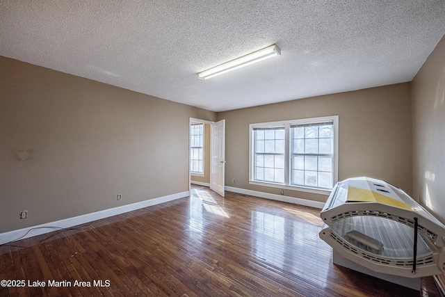 interior space with a textured ceiling, wood-type flooring, and baseboards