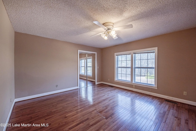 empty room with baseboards, visible vents, ceiling fan, dark wood-style flooring, and a textured ceiling