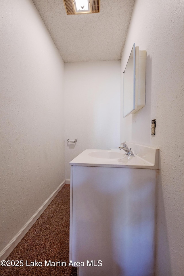 bathroom with baseboards, visible vents, a textured wall, a textured ceiling, and a sink