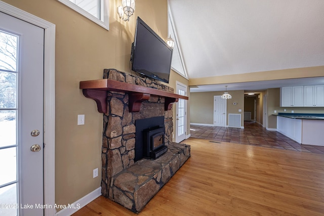 living area featuring lofted ceiling, a wood stove, a healthy amount of sunlight, and wood finished floors