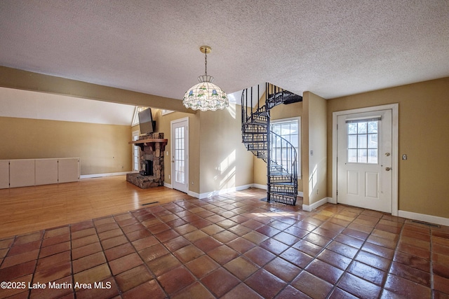 entrance foyer featuring a stone fireplace, baseboards, stairway, and a textured ceiling