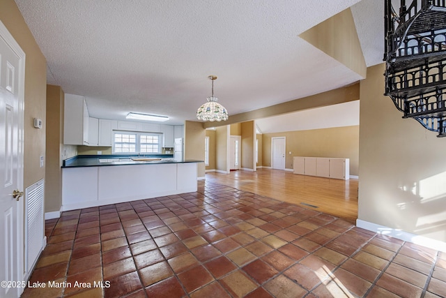 kitchen with a peninsula, white cabinetry, open floor plan, hanging light fixtures, and dark countertops