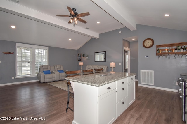 kitchen with vaulted ceiling with beams, white cabinets, a kitchen bar, a center island, and light stone countertops