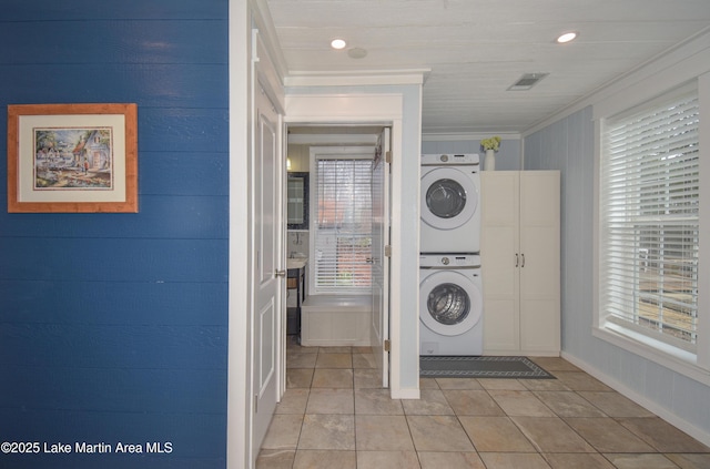 washroom featuring crown molding, plenty of natural light, stacked washer and clothes dryer, and light tile patterned flooring
