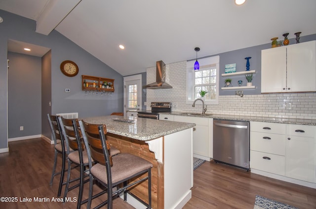 kitchen featuring wall chimney exhaust hood, white cabinetry, a center island, hanging light fixtures, and appliances with stainless steel finishes