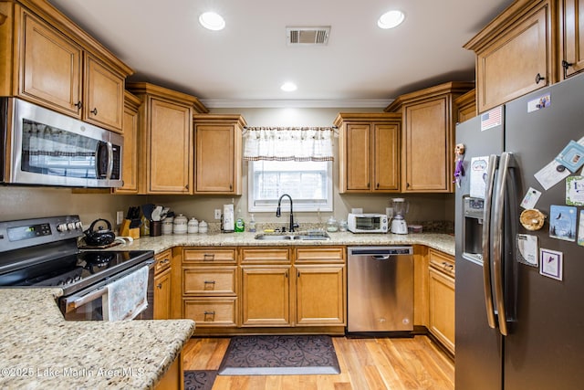 kitchen featuring a sink, stainless steel appliances, brown cabinetry, light wood-type flooring, and visible vents