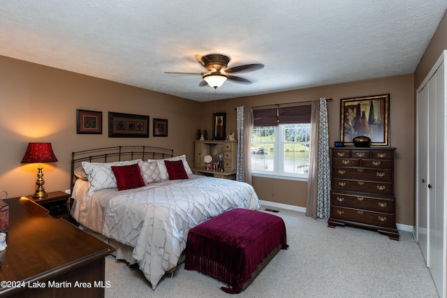 bedroom with a textured ceiling, ceiling fan, light carpet, and a closet