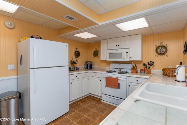 kitchen featuring a drop ceiling, white appliances, sink, tile countertops, and white cabinets