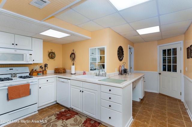 kitchen featuring kitchen peninsula, white appliances, white cabinets, and a paneled ceiling