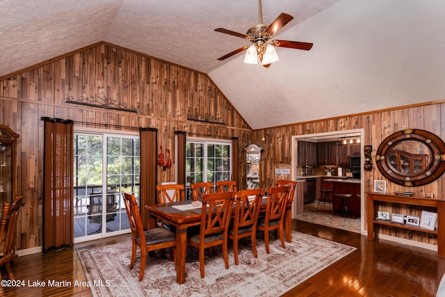 dining space with hardwood / wood-style flooring, wood walls, lofted ceiling, and a textured ceiling