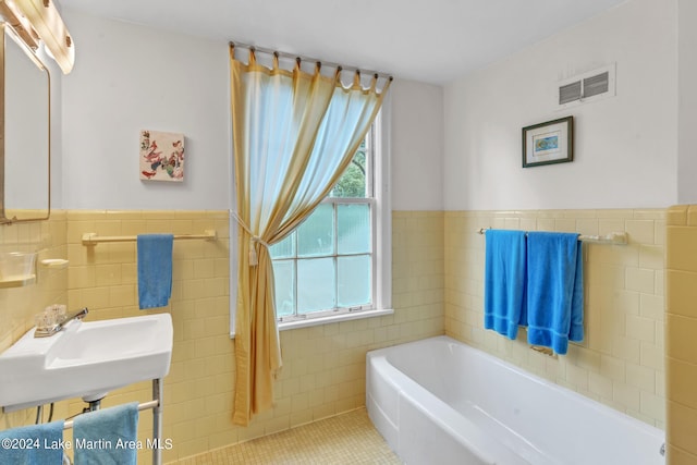 bathroom featuring tile patterned floors, a tub, sink, and tile walls