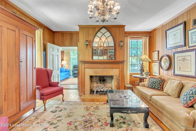 living room with wooden walls, a fireplace, wood-type flooring, and an inviting chandelier