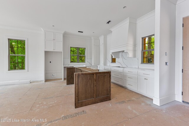 kitchen with a kitchen island, visible vents, crown molding, baseboards, and white cabinets
