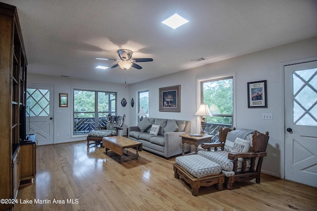 living room featuring ceiling fan, plenty of natural light, light hardwood / wood-style floors, and a textured ceiling