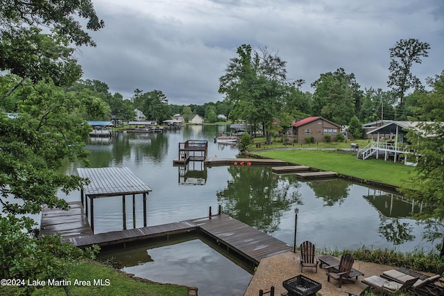 view of dock featuring a fire pit, a water view, and a lawn