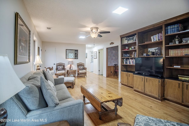 living room with ceiling fan, a textured ceiling, and light wood-type flooring