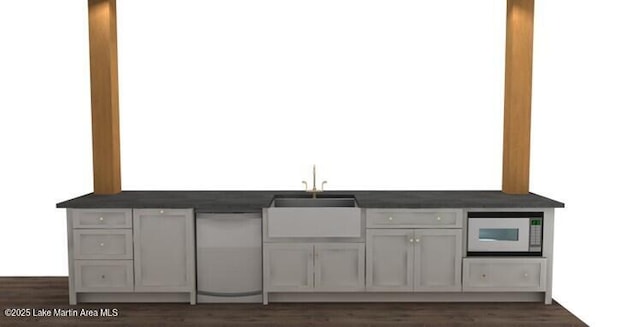 kitchen with dark countertops, dark wood finished floors, a sink, and white microwave