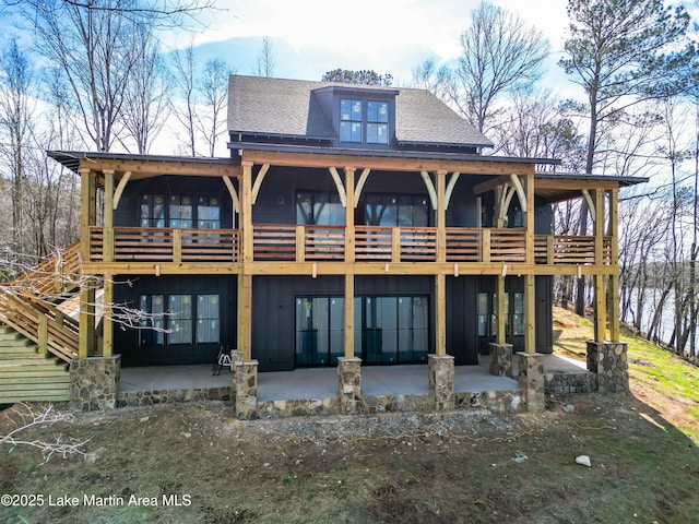 rear view of house with board and batten siding, a shingled roof, and a patio