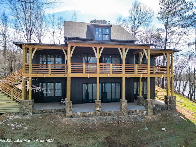 rear view of property featuring board and batten siding, roof with shingles, and a patio