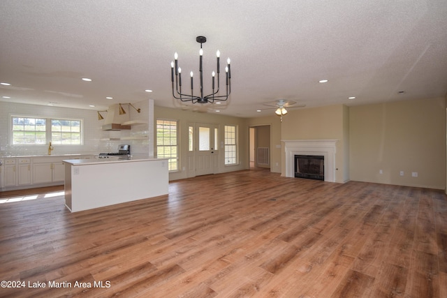 unfurnished living room with ceiling fan with notable chandelier, light wood-type flooring, and a textured ceiling