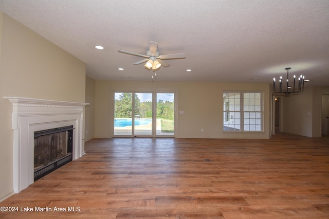 unfurnished living room with ceiling fan with notable chandelier, a textured ceiling, and hardwood / wood-style floors