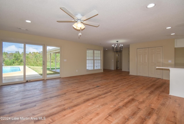 unfurnished living room with ceiling fan with notable chandelier, a textured ceiling, and light wood-type flooring