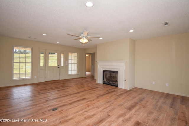 unfurnished living room with ceiling fan, a textured ceiling, and light hardwood / wood-style flooring