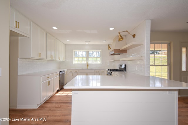 kitchen with kitchen peninsula, light hardwood / wood-style flooring, white cabinetry, decorative backsplash, and stainless steel appliances