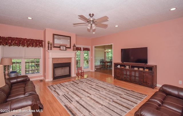 living room with ceiling fan with notable chandelier, plenty of natural light, light wood-type flooring, and a tile fireplace