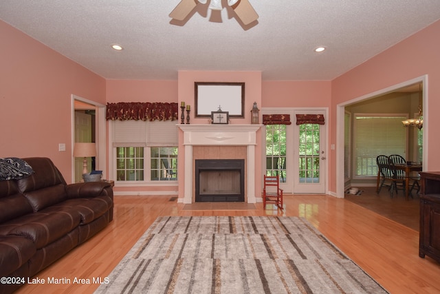living room with a tile fireplace, a textured ceiling, ceiling fan with notable chandelier, and light hardwood / wood-style floors