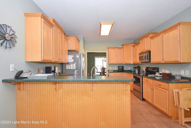 kitchen with kitchen peninsula, appliances with stainless steel finishes, light tile patterned floors, and light brown cabinetry