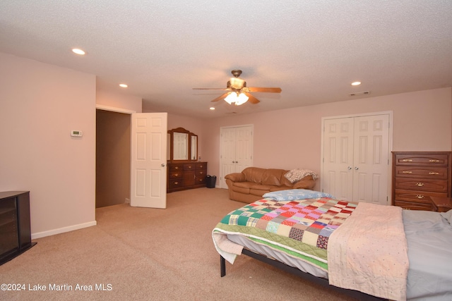 bedroom featuring two closets, ceiling fan, light colored carpet, and a textured ceiling