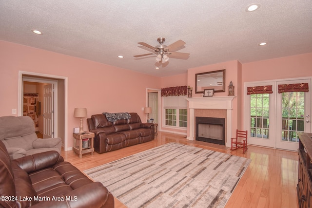 living room with a fireplace, a textured ceiling, light hardwood / wood-style flooring, and ceiling fan