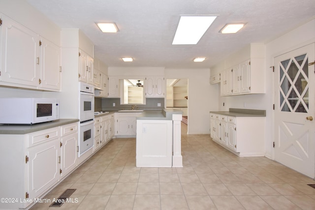 kitchen featuring a textured ceiling, white appliances, a kitchen island, sink, and white cabinetry