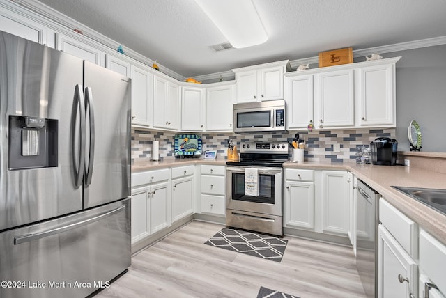 kitchen with tasteful backsplash, crown molding, white cabinets, and appliances with stainless steel finishes