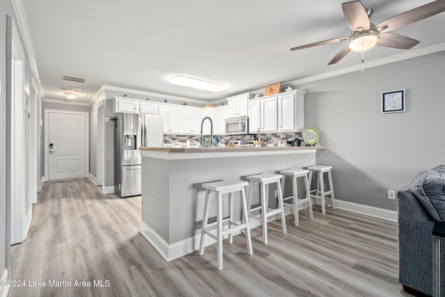 kitchen with kitchen peninsula, decorative backsplash, stainless steel appliances, crown molding, and white cabinetry