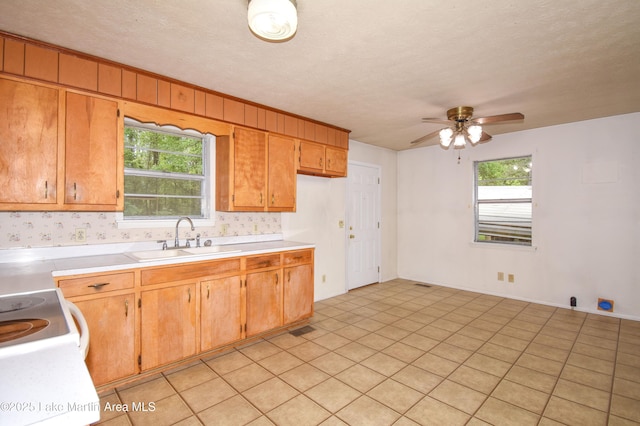 kitchen with light countertops, a ceiling fan, a sink, brown cabinetry, and a textured ceiling