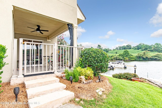 doorway to property featuring ceiling fan, a yard, and a water view