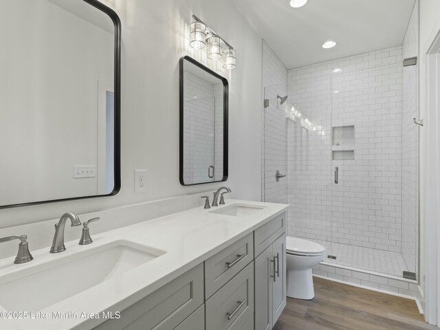 full bathroom with double vanity, wood finished floors, a sink, and a shower stall