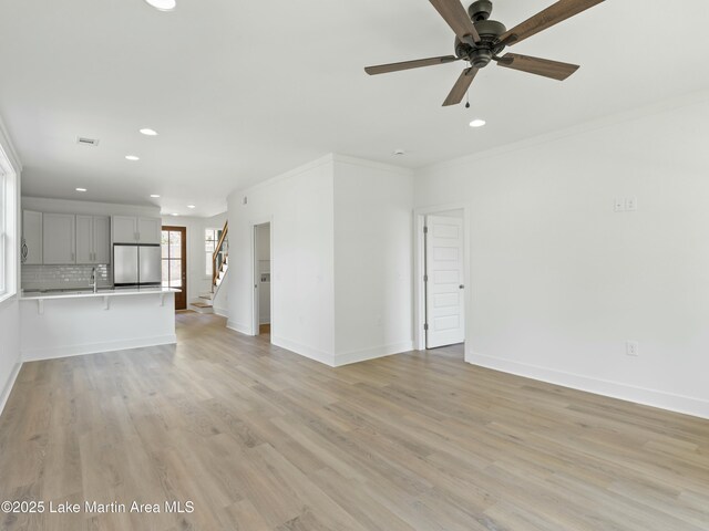 unfurnished living room featuring light wood-style flooring, stairs, baseboards, and ornamental molding