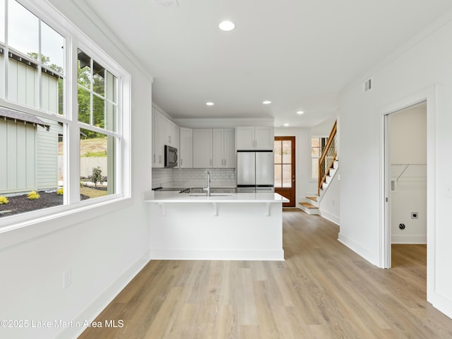 kitchen with light countertops, decorative backsplash, appliances with stainless steel finishes, a sink, and a peninsula