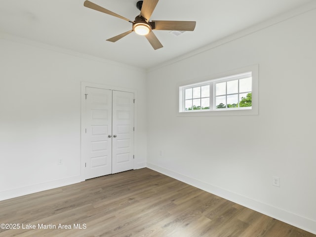 spare room with a ceiling fan, crown molding, baseboards, and wood finished floors