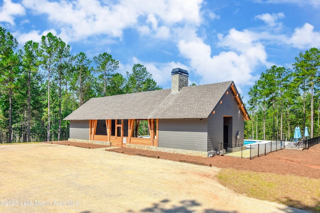 view of front of house featuring fence, a fenced in pool, roof with shingles, and a chimney