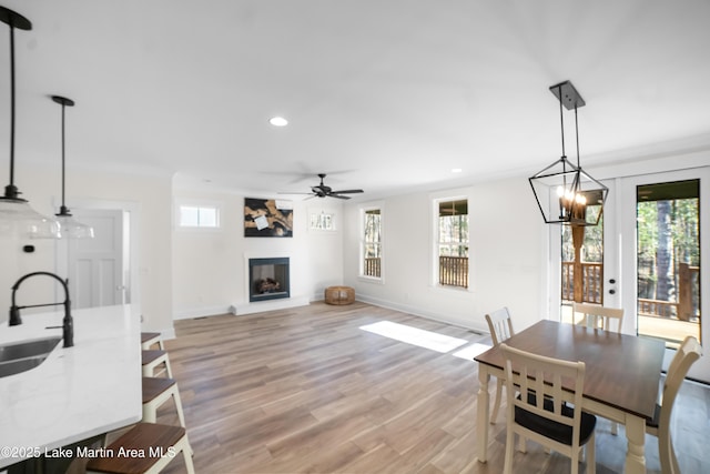 dining space with a fireplace with raised hearth, baseboards, recessed lighting, light wood-style floors, and a ceiling fan