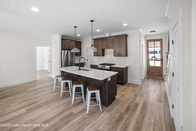 kitchen featuring stainless steel appliances, a sink, dark brown cabinets, light wood-style floors, and a kitchen bar