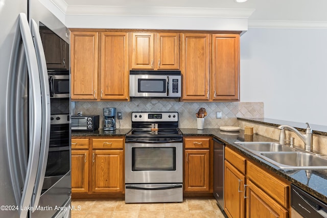 kitchen with appliances with stainless steel finishes, dark stone counters, tasteful backsplash, sink, and ornamental molding