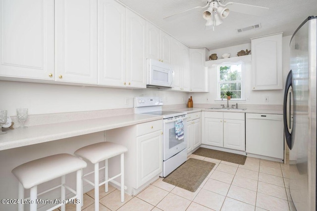 kitchen with a breakfast bar, white appliances, white cabinets, sink, and light tile patterned flooring