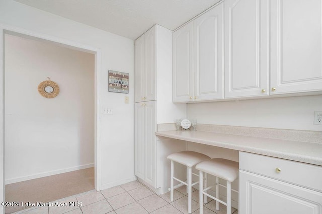 kitchen with built in desk, white cabinetry, and light tile patterned floors