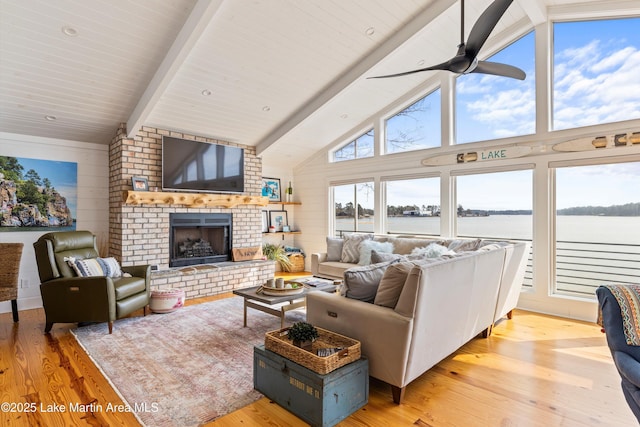 living area featuring high vaulted ceiling, a fireplace, a ceiling fan, light wood-type flooring, and beamed ceiling