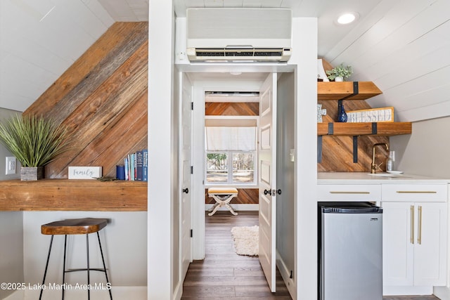 interior space with wooden walls, a sink, wood finished floors, vaulted ceiling, and a wall mounted AC